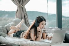 a woman laying on her bed using a laptop and headphones to listen to music