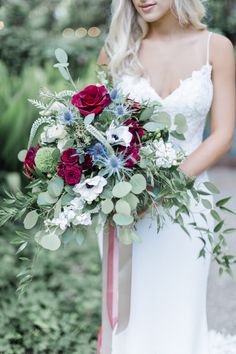 a bride holding a bouquet of red and white flowers in her hand with greenery