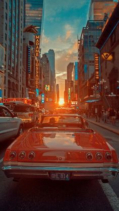 an old red car is parked in the middle of a busy city street at sunset