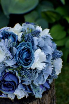 a bouquet of blue and white flowers sitting on top of a tree stump