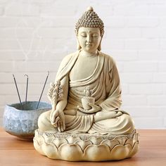 a buddha statue sitting on top of a wooden table next to a potted plant