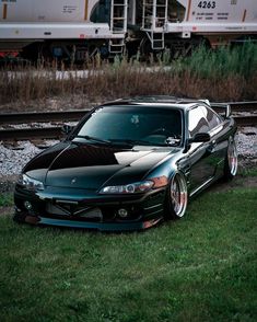 a black sports car parked in front of a train on the tracks next to grass