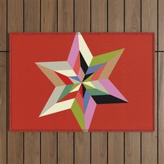 a red area rug with a multicolored star design on the floor next to wood planks