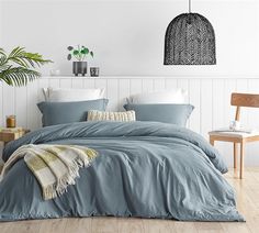 a bed with blue sheets and pillows in a white room next to a wooden chair