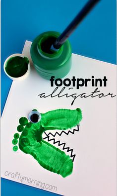 a paper plate with a handprinted alligator on it next to a cup of green paint