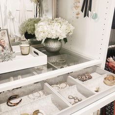 a white dresser with jewelry on it and a vase filled with flowers in the background