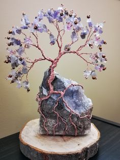 a rock with a wire tree on it sitting on top of a wooden stump next to a wall