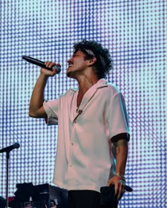 a male in a white shirt and black pants singing into a microphone at a concert