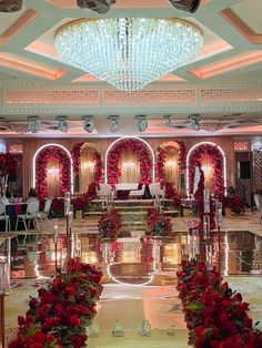 an elaborately decorated hall with chandeliers and red flowers on the tables in front of it