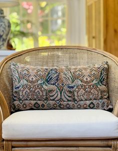 a wicker chair with a cushion on it in front of a window and vase