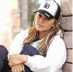 a woman sitting against a brick wall wearing a white and black hat with the letter b on it