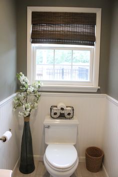 a white toilet sitting in a bathroom next to a window with shades on the windowsill