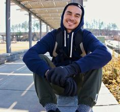 a man sitting on top of a skateboard in front of a covered area with bushes