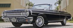 an old black car is parked in front of a building with palm trees behind it