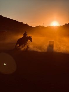 a person riding on the back of a horse in an open field at sunset or sunrise