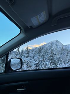 the view from inside a car looking at snow covered mountains and trees in the distance