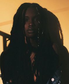 a woman with dreadlocks standing in front of a yellow wall