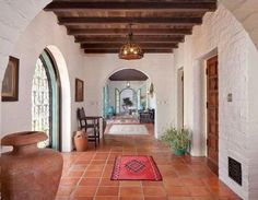 a hallway with red tiles and potted plants on the floor, along with arched doorways