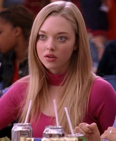 a woman sitting at a table with two drinks in front of her and another person behind her