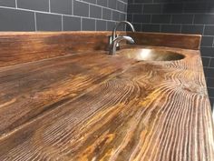 a wooden counter top in a bathroom next to a sink and tiled wall behind it