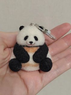 a small stuffed panda bear sitting on top of a persons hand with a keychain