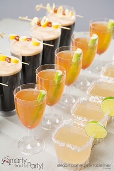 several glasses filled with drinks and garnished with limes on a white table