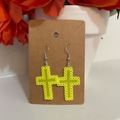 a pair of yellow cross earrings sitting on top of a flower pot next to a plant