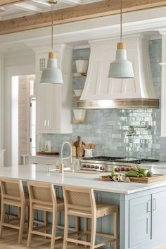 a large kitchen with an island and several chairs around the countertop, along with two pendant lights hanging from the ceiling