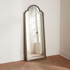 a mirror sitting on the floor in front of a white wall with a window behind it