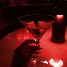 a person is holding a martini glass in front of a lit candle on a table