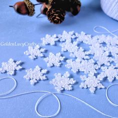 white snowflakes are sitting on a blue surface next to yarn and pine cones