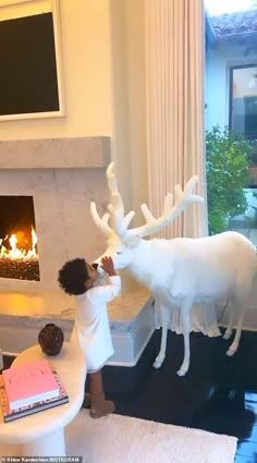 a little boy standing next to a fake reindeer in front of a fire place with a cake on it