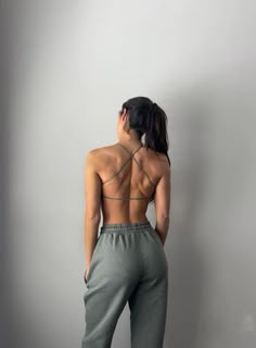 a woman with her back turned to the camera, wearing grey sweatpants and a bra