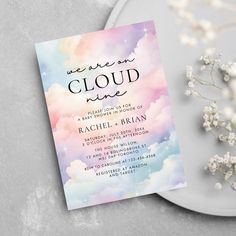 a watercolor cloud baby shower is on the table next to flowers and a white plate