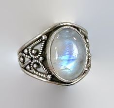 "This is a beautiful Bali, ethnic style, stunning, sterling silver vintage ring!  A beautiful glowing oval shaped moonstone is the centerpiece of this vintage bohemian ring! The stone flashed with shades of gorgeous blue.  Done in sterling silver, the moonstone is accented by a wide Bali style silver setting.  The stone sits up from the setting to catch the light.  The setting is ornate with an ornate sterling design.  This beauty is sure to be noticed upon you finger!  Condition: Very good vint Bohemian Oval Cabochon Moonstone Ring, Silver Bohemian Moonstone Cabochon Ring, Silver Cabochon Moonstone Ring In Bohemian Style, Silver Oval Moonstone Ring With Intricate Design, Bohemian Sterling Silver Oval Cabochon Moonstone Ring, Bohemian Oval Moonstone Ring, Bohemian Silver Moonstone Ring In Oval Cabochon, Bohemian Silver Oval Cabochon Moonstone Ring, Bohemian Silver Moonstone Cabochon Ring