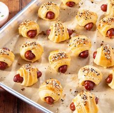 hot dogs wrapped in bread and topped with sesame seeds are ready to be eaten on a baking sheet