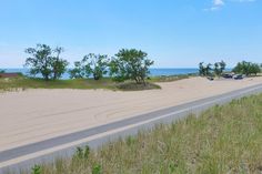 an empty road near the beach with cars parked on it and trees in the distance