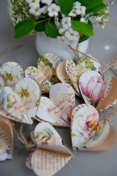 some paper hearts are sitting next to a vase with flowers in it and tags attached to them