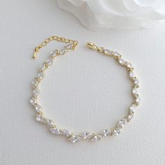 a gold bracelet with crystal beads and a rose on the side, next to it is a white flower