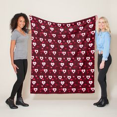 two women standing next to each other holding up a black and red heart print blanket