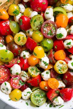 a white bowl filled with tomatoes, mozzarella and other veggies next to a wooden spoon