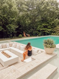 a woman sitting on the edge of a large couch next to a swimming pool with trees in the background