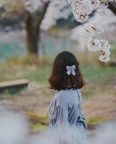 a woman with a bow in her hair standing next to a tree filled with white flowers