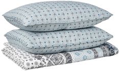 three pillows stacked on top of each other in blue and white patterns, with one pillow folded up to the side