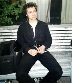 a young man sitting on a bench in front of a window with his luggage behind him