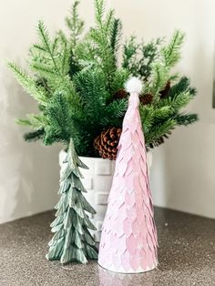 two small christmas trees sitting next to each other on top of a table with pine cones