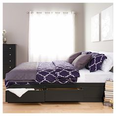 a bed with purple sheets and pillows in a room next to a dresser, window