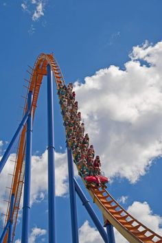 a roller coaster ride with people riding on it's side and clouds in the background