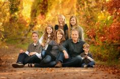 a family sitting on the ground in front of trees with fall leaves around them and smiling at the camera