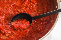 a ladle full of red sauce being stirred by a spoon